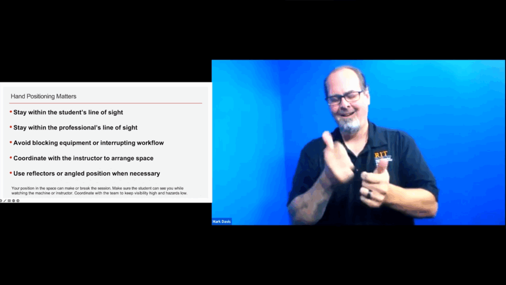 A presentation slide titled "Hand Positioning Matters" is displayed on the left, listing four key guidelines for sign language interpreters, such as staying within the line of sight and avoiding the blocking of equipment. On the right, an interpreter identified as Mark Davis, wearing an RIT-branded shirt, is actively signing against a bright blue background. The slide's footnote emphasizes the importance of coordinating with the team to ensure high visibility and low hazards when interpreting near machinery.
