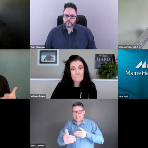 A screenshot of a virtual panel discussion shows seven participants arranged in a grid layout against various office or solid color backgrounds. The group features moderator Corey Axelrod, panelists Shana Ames, Valoree Boyer, Sara Jodi, and Scott Jeffery (who is actively signing), alongside ASL/English interpreters Cain Chiasson and Aaryn Adams.
